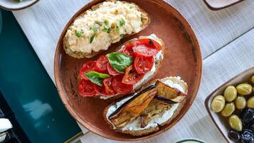 A plate with three open-faced sandwiches, one with a creamy spread, another with tomato slices and basil, and the third with roasted eggplant and a creamy spread.