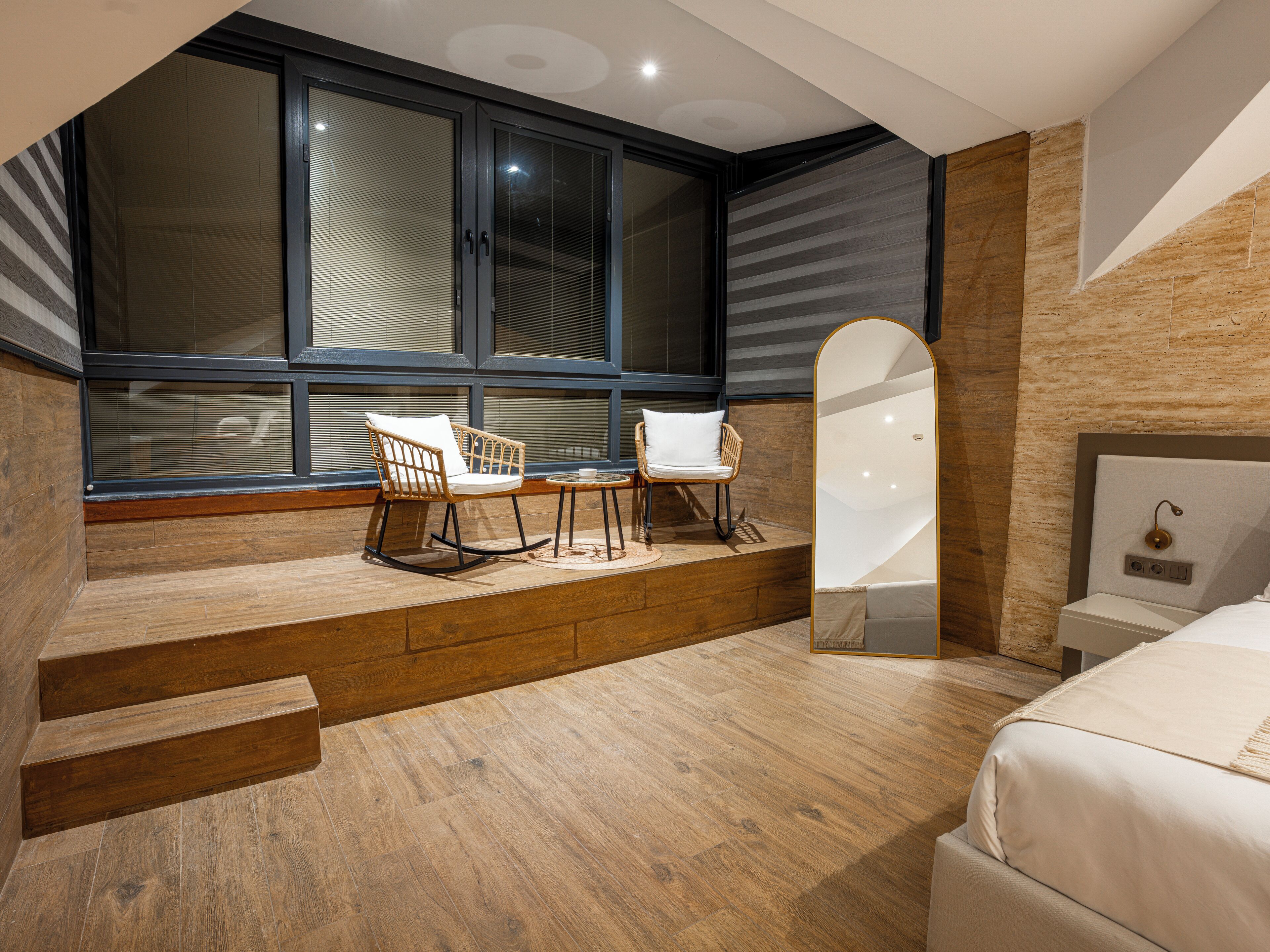 A modern bedroom with a large window, a bed, a chair, and a mirror.
