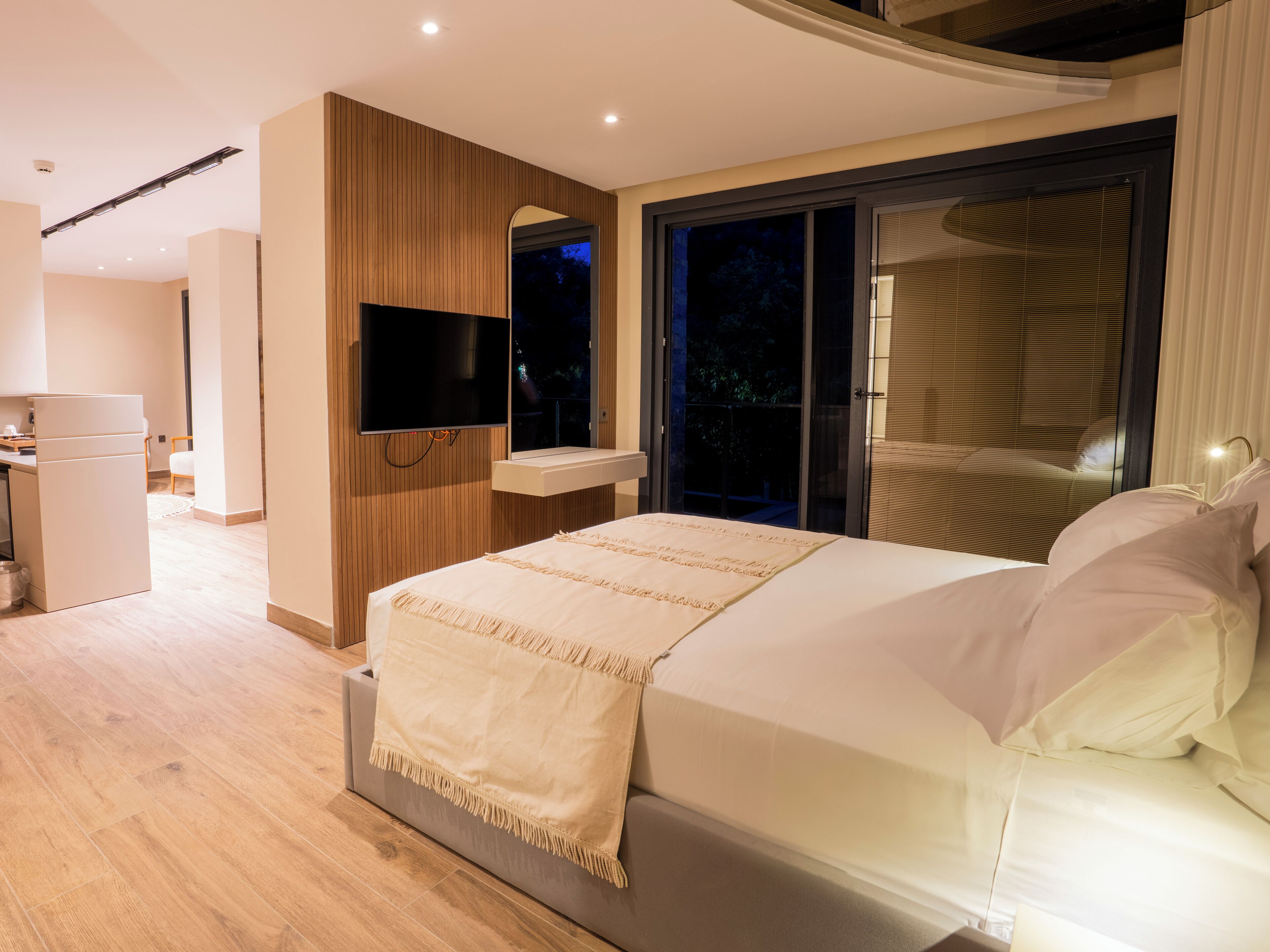 Een moderne slaapkamer met een groot bed, een flatscreen televisie aan de wand en een raam met jaloezieën.