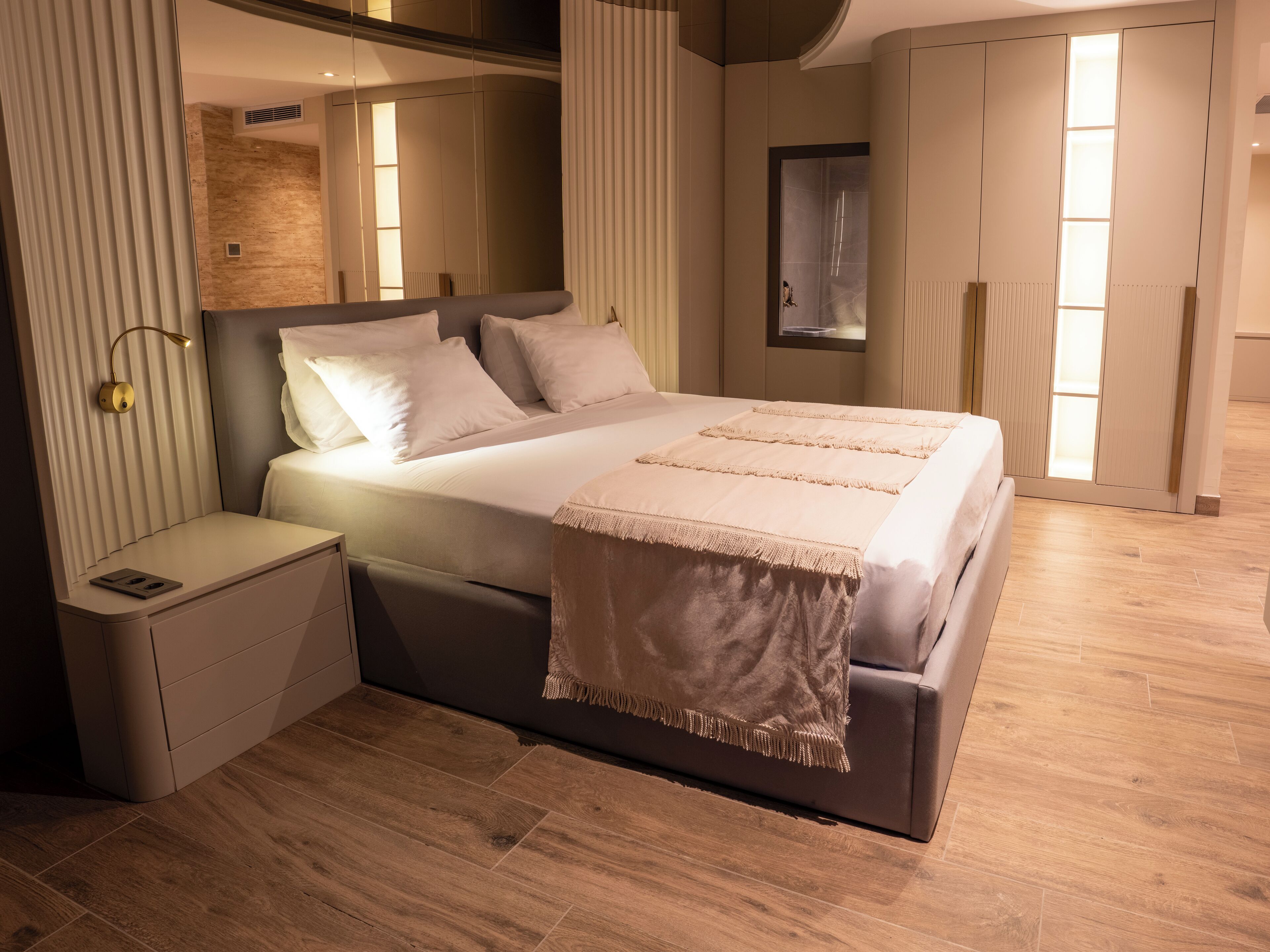 Un dormitorio moderno con una cama grande, mesitas de noche, un espejo y un armario.