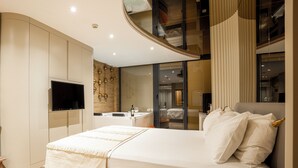 A modern bedroom with a large bed, a TV mounted on the wall, and a bathroom visible through a glass partition. - Verona Hotel (Sile)