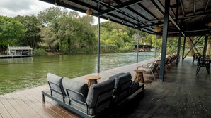 A covered outdoor seating area with a view of a river and greenery. - Verona Hotel (Sile)