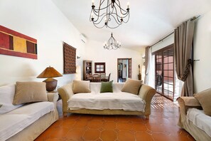 A living room with a sofa, a lamp, a chandelier, and a view through a glass door.