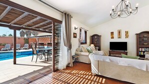 Una sala de estar con sofá, televisor y un área de piscina con sillas y mesa.