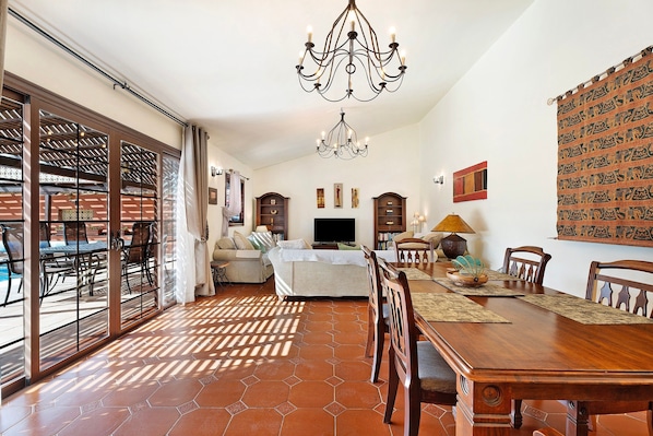 A spacious living area with a dining table, chairs, a sofa, a TV, and a patterned wall.