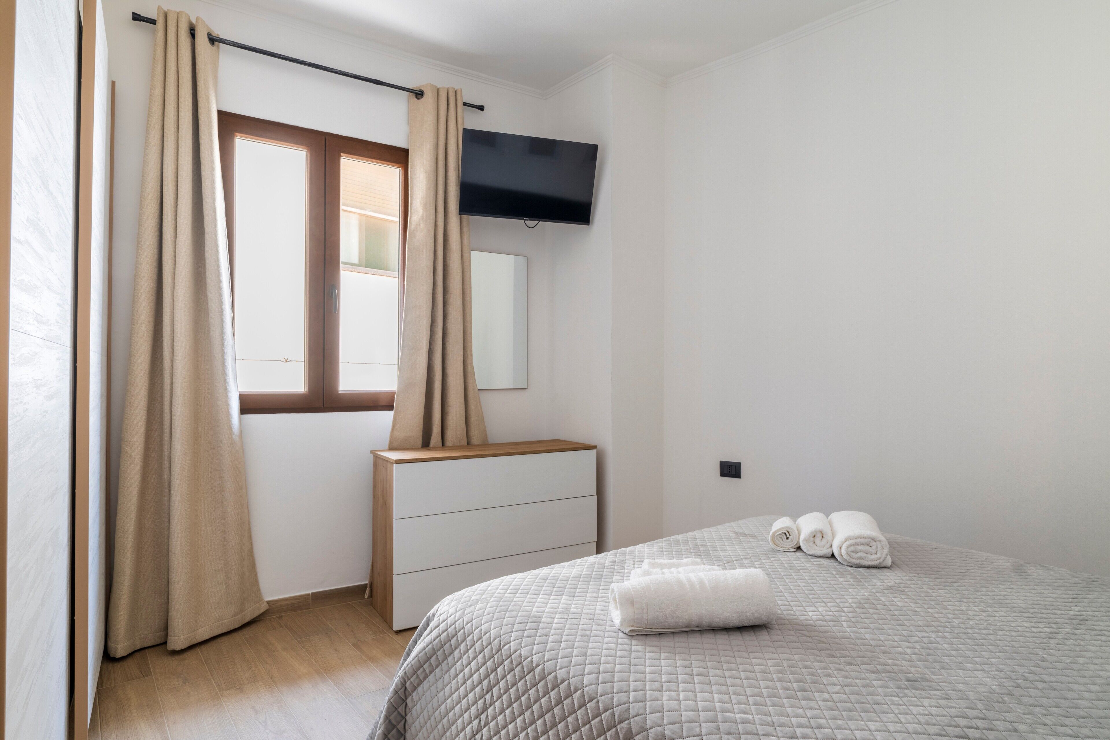 Un dormitorio con cama, cómoda, espejo y ventana con cortinas.