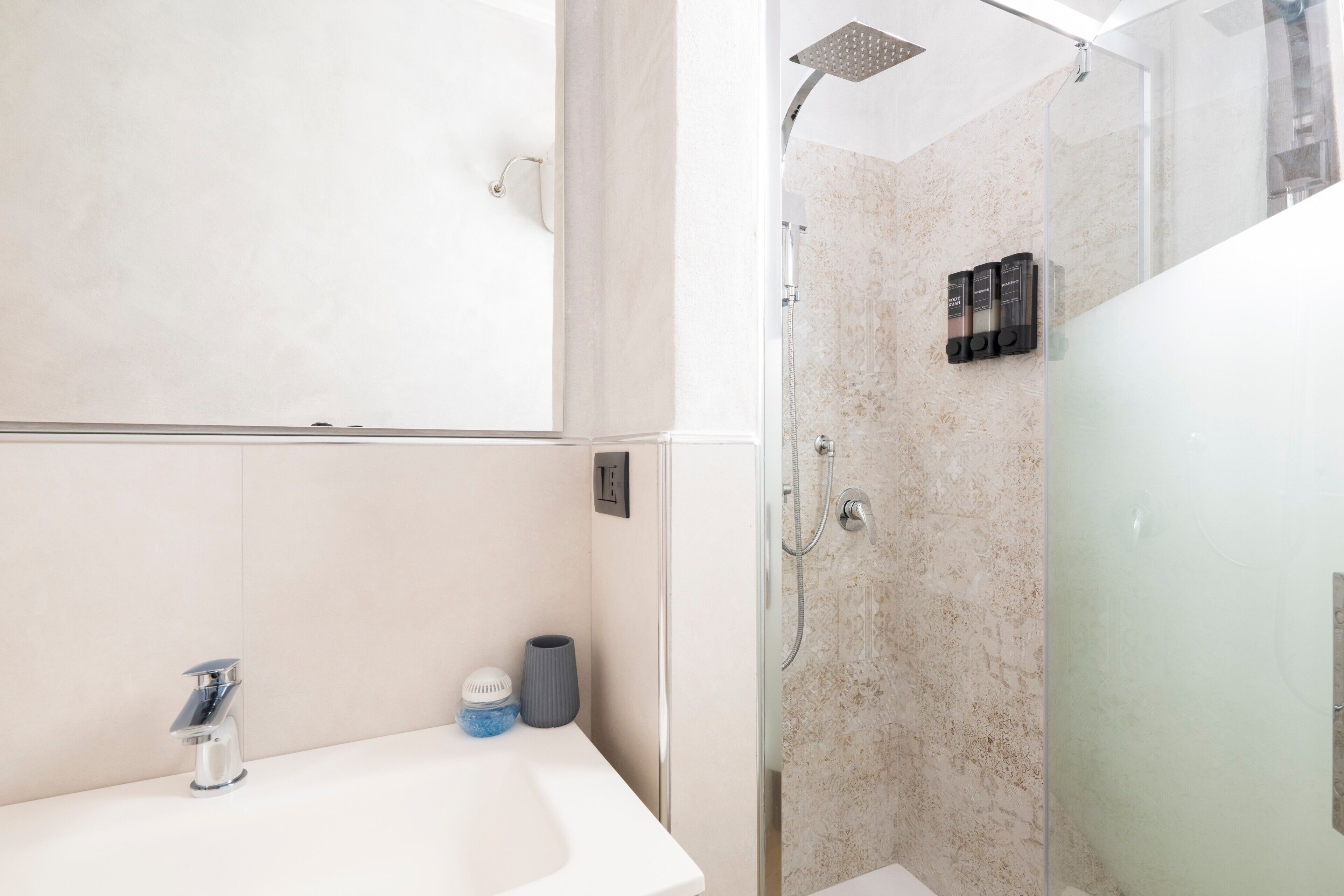 A bathroom with a white sink, a mirror, a shower with a glass door, and a marble wall.