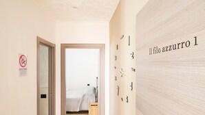 Un pasillo con una cama al fondo, una puerta con el letrero de prohibido fumar, y una pared con números.