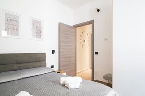 A modern bedroom with a bed, a bedside table, a wall clock, and two framed pictures.