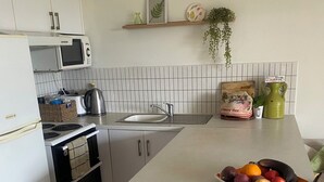 A kitchen with white cabinets, a microwave, a kettle, a sink, and a fruit bowl on the counter. - Tropical views from spacious, comfortable, well appointed apartment (Palm Cove)
