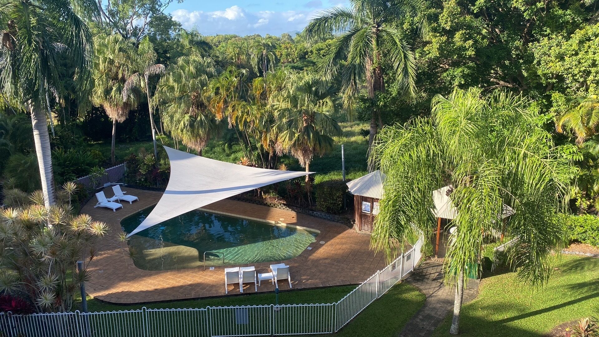 A pool area with lounge chairs and a shaded canopy, surrounded by lush greenery.