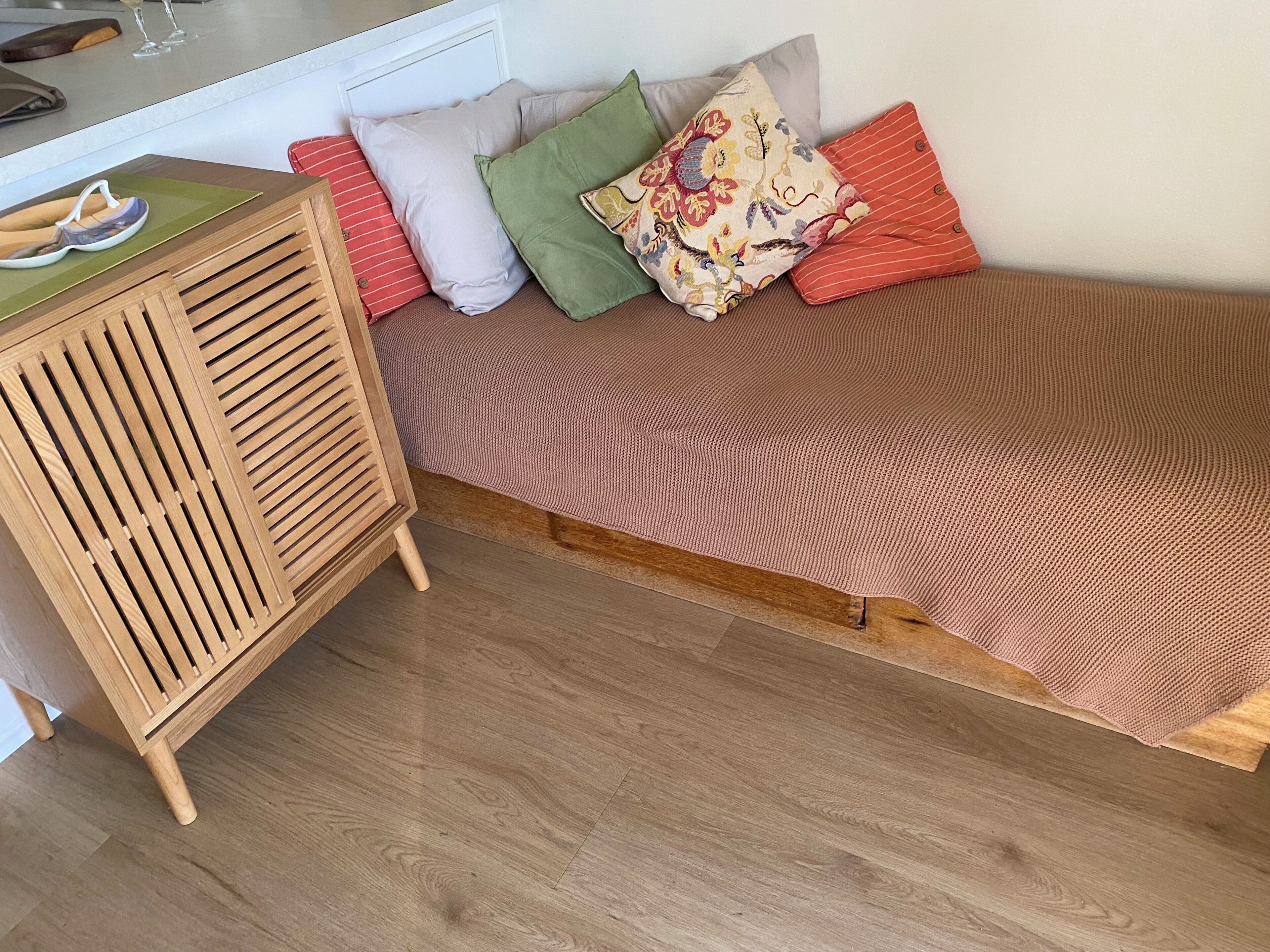 A small, cozy room with a wooden cabinet, a bed with a patterned bedspread, and several pillows.