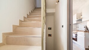 Un escalier menant à une cuisine dotée de meubles blancs et d’un dosseret en marbre.