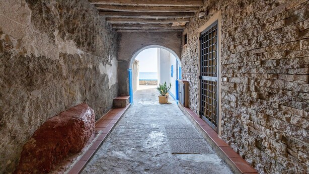A narrow corridor with stone walls, a wooden bench, and a potted plant. - Aurora Sul Mare Apartment with Wi-Fi and Air Conditioning (Palermo)