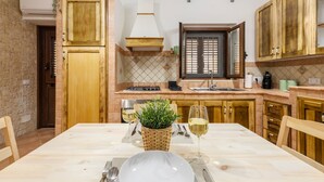 A kitchen with wooden cabinets, a tiled backsplash, a dining table with chairs, and a potted plant. - Aurora Sul Mare Apartment with Wi-Fi and Air Conditioning (Palermo)