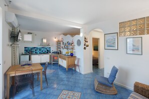 Un espacio habitable compacto con comedor, cocina y zona de estar con una silla y cojines.