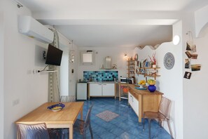 Une cuisine compacte avec un crédence carrelée, un coin repas avec des chaises, un petit réfrigérateur et un téléviseur à écran plat fixé au mur.