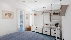 Ein Schlafzimmer mit einem Bett, einer weißen Kommode, Regalen und einem Kleiderschrank.