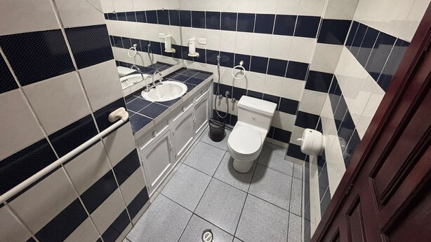 A bathroom with a sink, toilet, and shower. The walls are tiled with a black and white pattern. - Hotel del mall (Ambato)