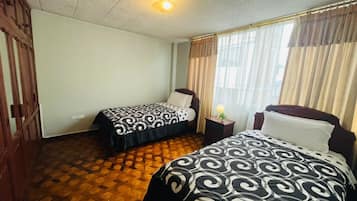 Habitación de hotel con dos camas, piso de madera, una lámpara en el techo y una ventana con cortinas.