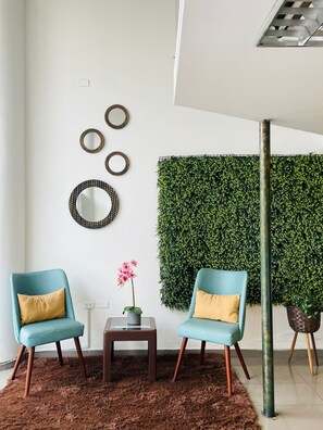 A modern living room with two teal armchairs, a small side table, a decorative mirror, a green wall panel, and a potted plant. - Hotel del mall (Ambato)