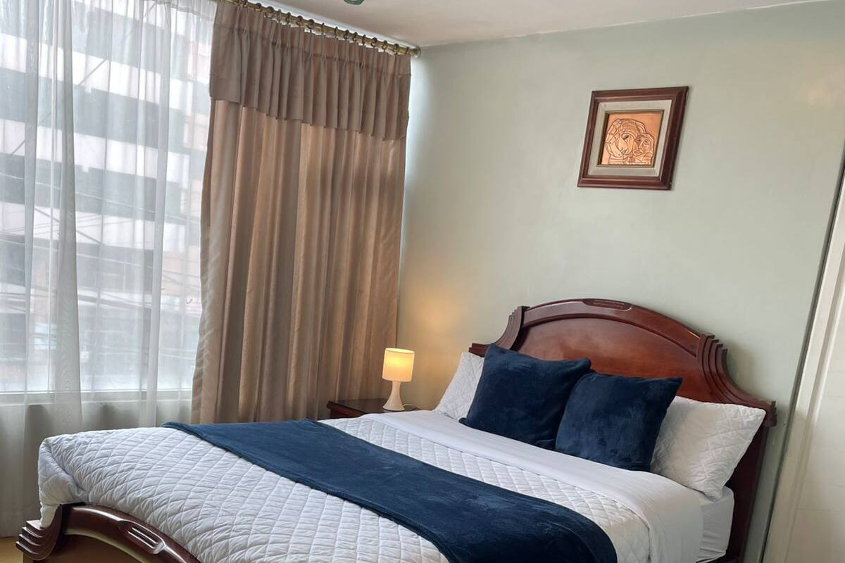 A neatly made bed with a wooden headboard, a fluffy rug, and a lamp on a bedside table.