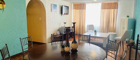 A dining area with a round table, chairs, a television, and a cabinet.