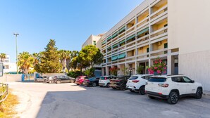Ein Parkplatz mit mehreren Autos, ein Mehrfamilienhaus mit Balkonen und Palmen.