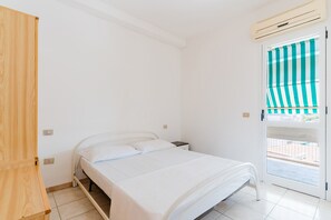 Ein Schlafzimmer mit einem Bett, einem Holzschrank, einem Nachttisch und einer Tür mit gestreiftem Jalousievorhang.