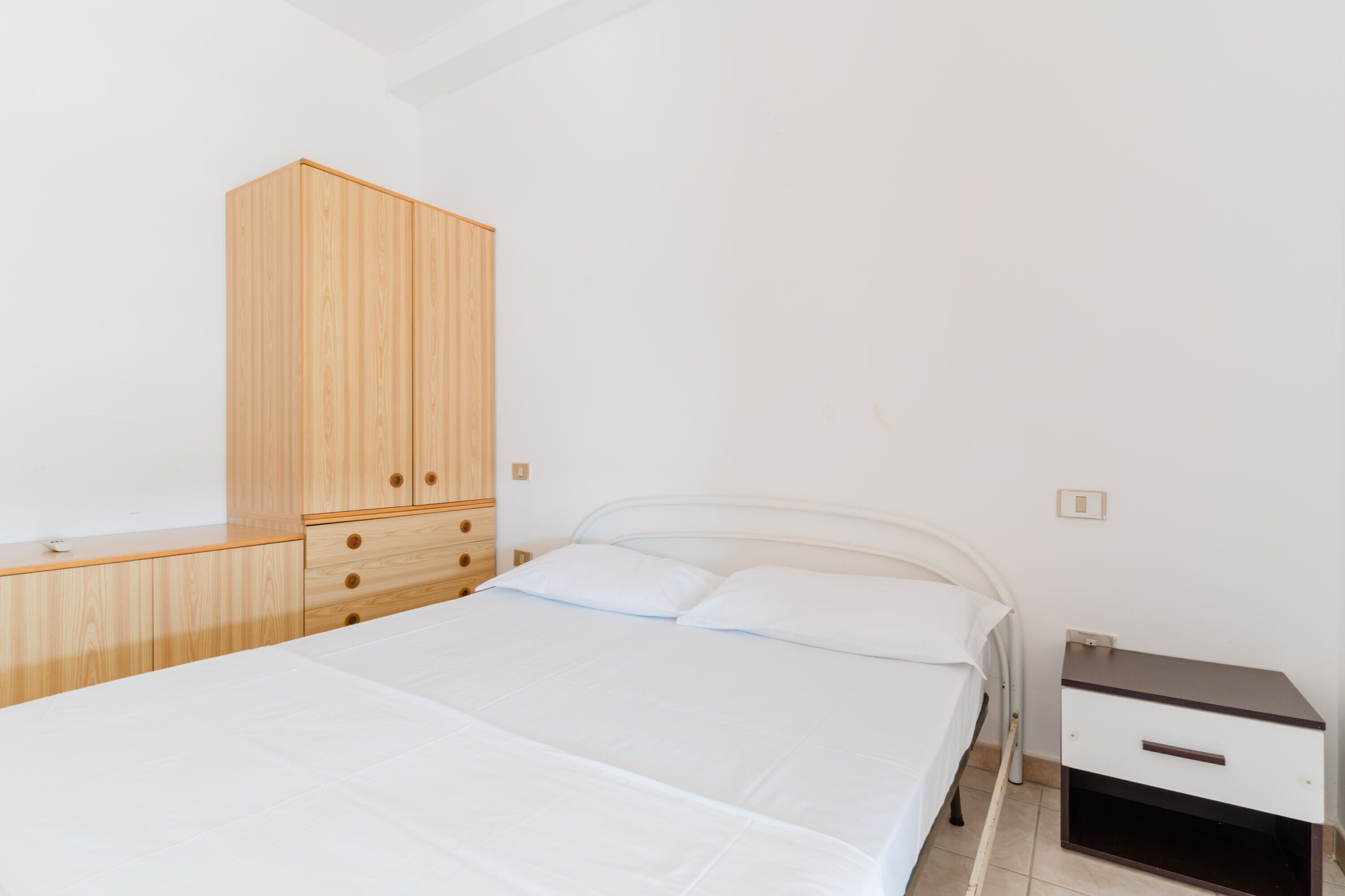 A bedroom with a bed, wooden wardrobe, and a bedside table.