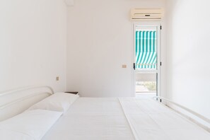 Ein Schlafzimmer mit einem Bett, einem Fenster mit gestreifter Vorhang und einer Klimaanlage.