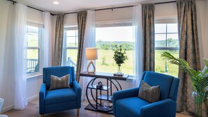 Una habitación con dos sillones azules, una mesita con lámpara y vistas al exterior con vegetación.