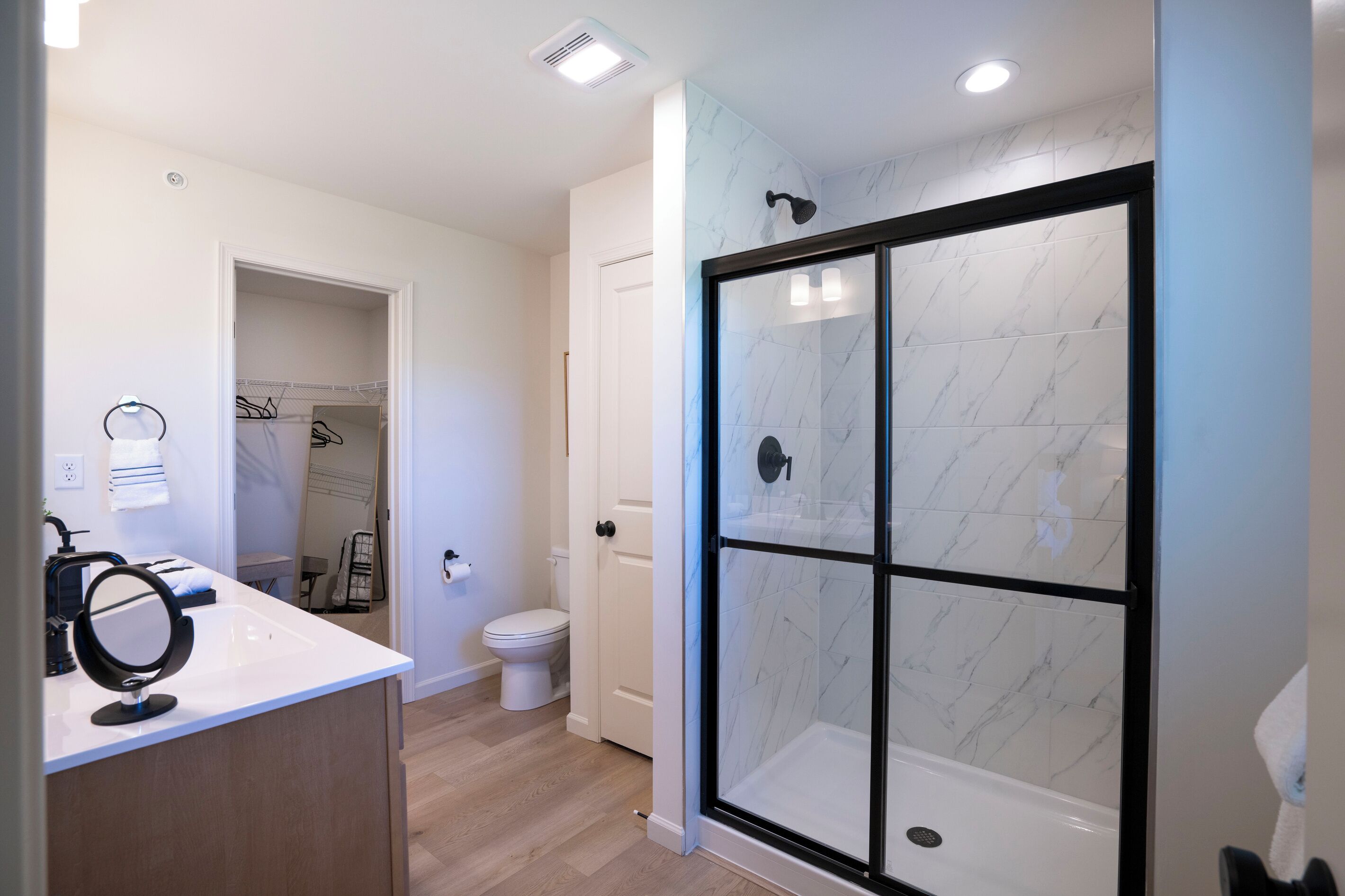 A modern bathroom with a glass-enclosed shower, a toilet, and a vanity with a mirror.