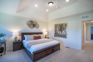 A bedroom with a large bed, bedside tables, a wall-mounted artwork, and a ceiling light fixture.