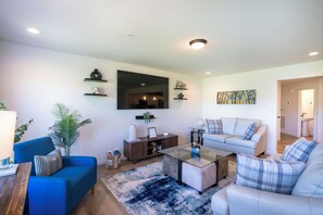 A living room with a sofa, armchair, coffee table, and a TV on the wall.