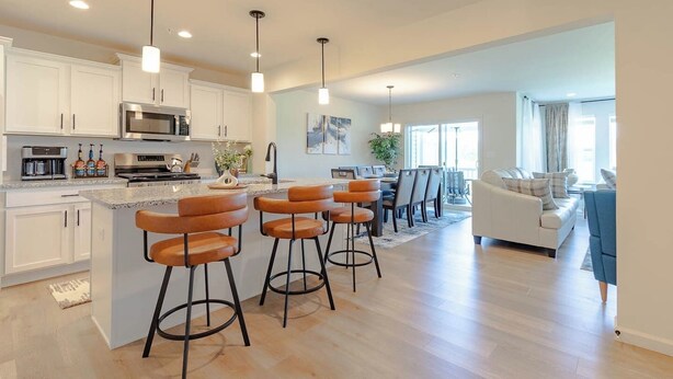 Una cocina moderna con armarios blancos, una isla central con taburetes de bar, electrodomésticos de acero inoxidable e iluminación colgante.