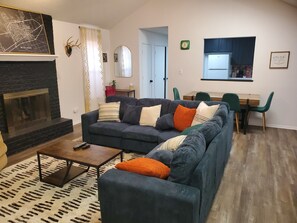 A living room with a dark blue sofa, a fireplace, a dining area with a table and chairs, and a kitchen visible through an open door. - Welcome to your Permian Paradise! Close to everything Midland has to offer... (Midland)