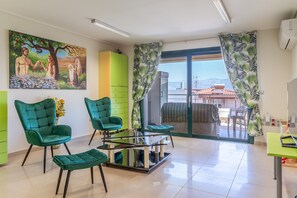 Uma sala de estar moderna com uma mesa de vidro, cadeiras verdes, um armário verde e um quadro na parede.