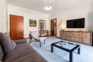 A living room with a sofa, armchair, coffee table, TV, bookshelf, and a cabinet.