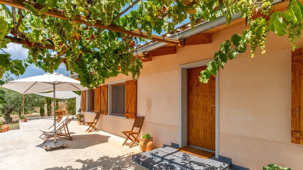 A building with a wooden pergola, outdoor seating, and a door. - Country House 'Lluna' with Mountain View, Shared Pool and Wi-Fi (Ibi)