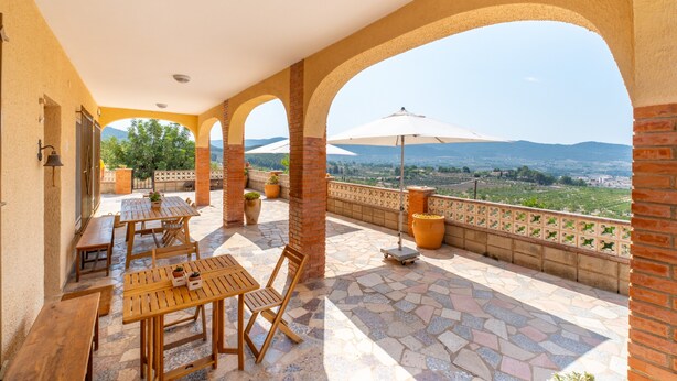 A covered outdoor patio with tables and chairs, a view of the countryside, and a brick wall. - Country House 'Sol' with Mountain View, Shared Pool and Wi-Fi (Ibi)