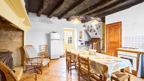 Comedor con una mesa dispuesta para cuatro personas, rodeado de sillas de madera, una chimenea y una zona de cocina con estufa y microondas.