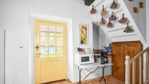 Una cocina con una puerta amarilla, una mesa blanca con electrodomésticos, y una escalera de madera.