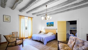 Una habitación con una cama, dos sillas, un sofá, suelo de madera, techo con vigas a la vista y un cuadro en la pared.