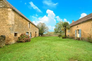 Une cour bordée de bâtiments en pierre, une pelouse verdoyante et un ciel bleu azur.