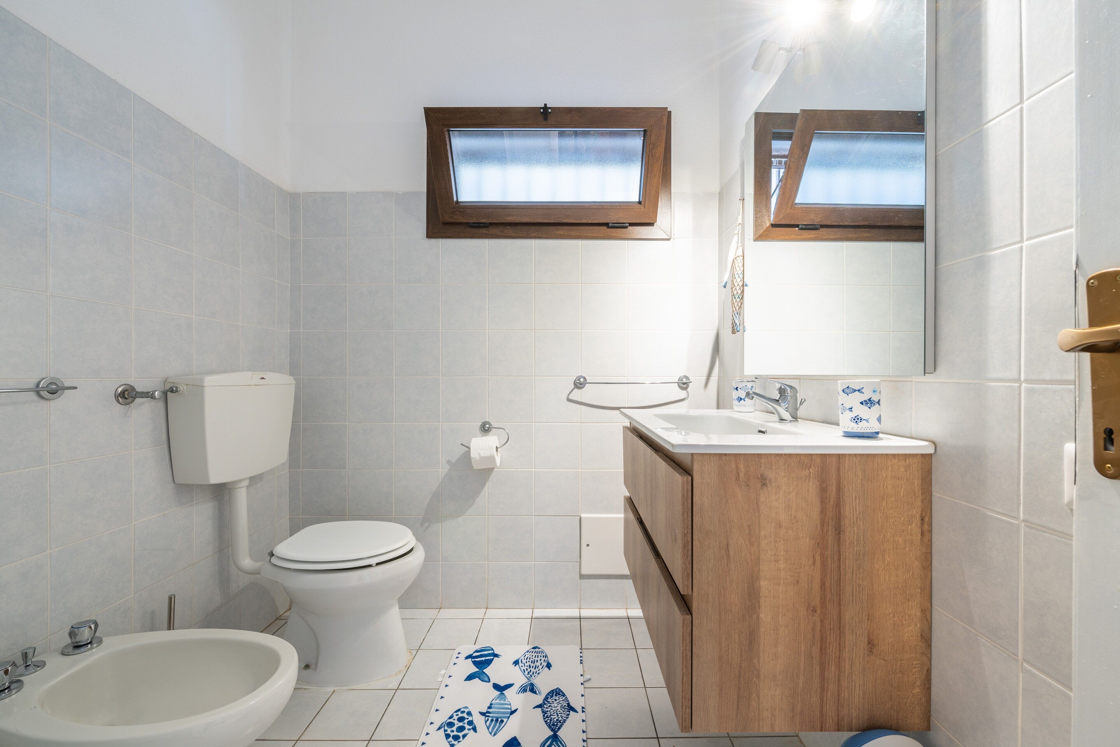 Ein Badezimmer mit Toilette, Bidet, Waschbecken, Holzkommode und einem Fenster mit Blick.
