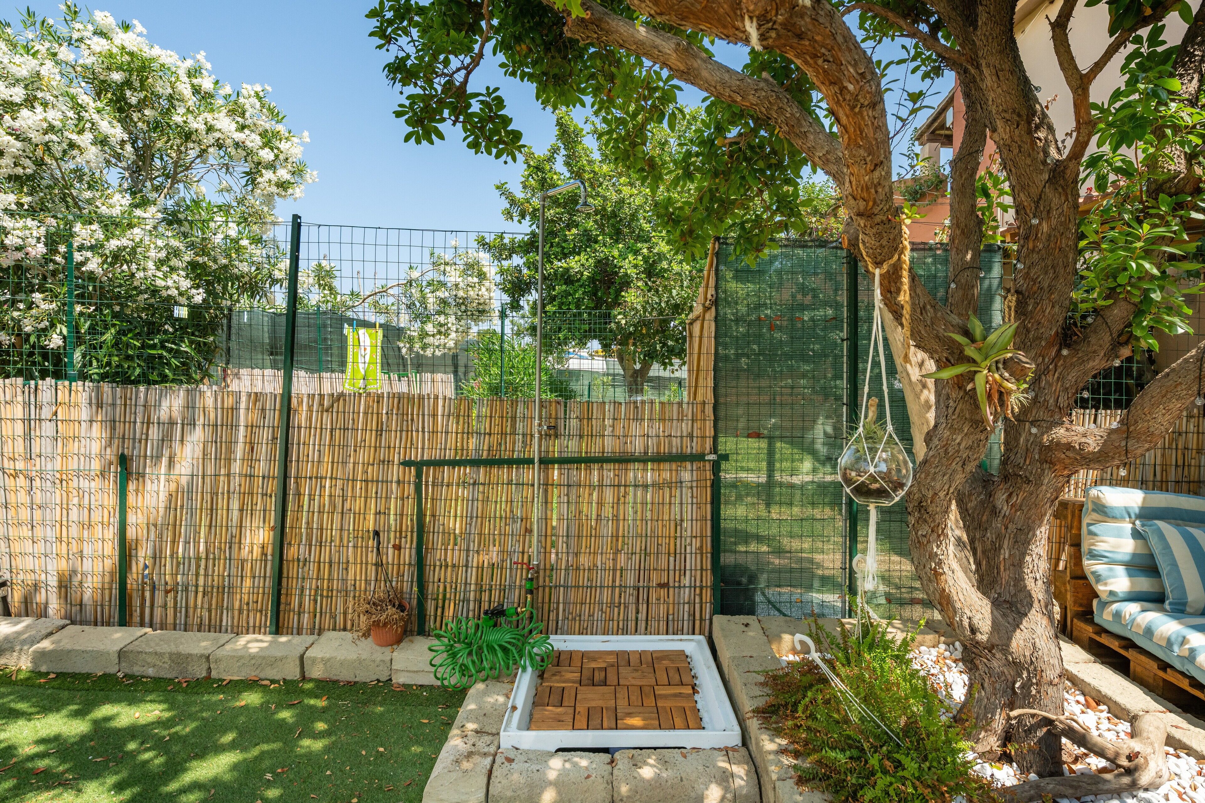 Un patio trasero cercado con una jardinera de madera, un árbol y una banca.