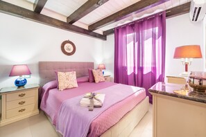 A bedroom with a bed, two bedside tables, a nightstand, a window with purple curtains, and a wall-mounted air conditioner. - Apartment 'Casa Di Design A' with Private Terrace, Wi-Fi and Air Conditioning (Calasetta)