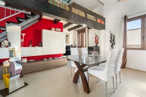 A modern kitchen with a glass dining table, white chairs, and a red accent wall.