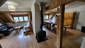 Amplia zona de estar tipo loft con chimenea, vigas de madera, una mesa de comedor y una cocina.